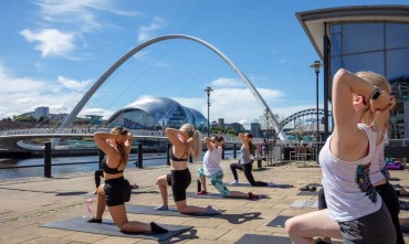 A group of women doing yoga on Newcastle’s Quayside with the Millennium Bridge in the background