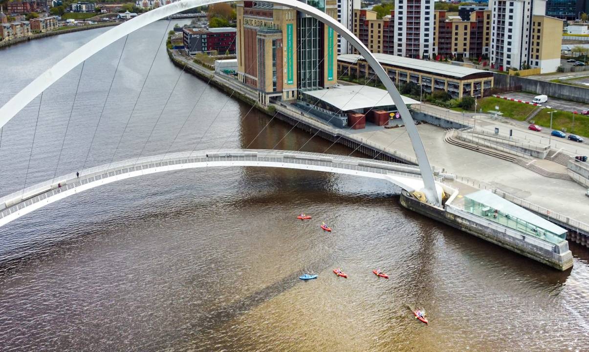 A group of people kayaking on the River Tyne near the Millennium Bridge