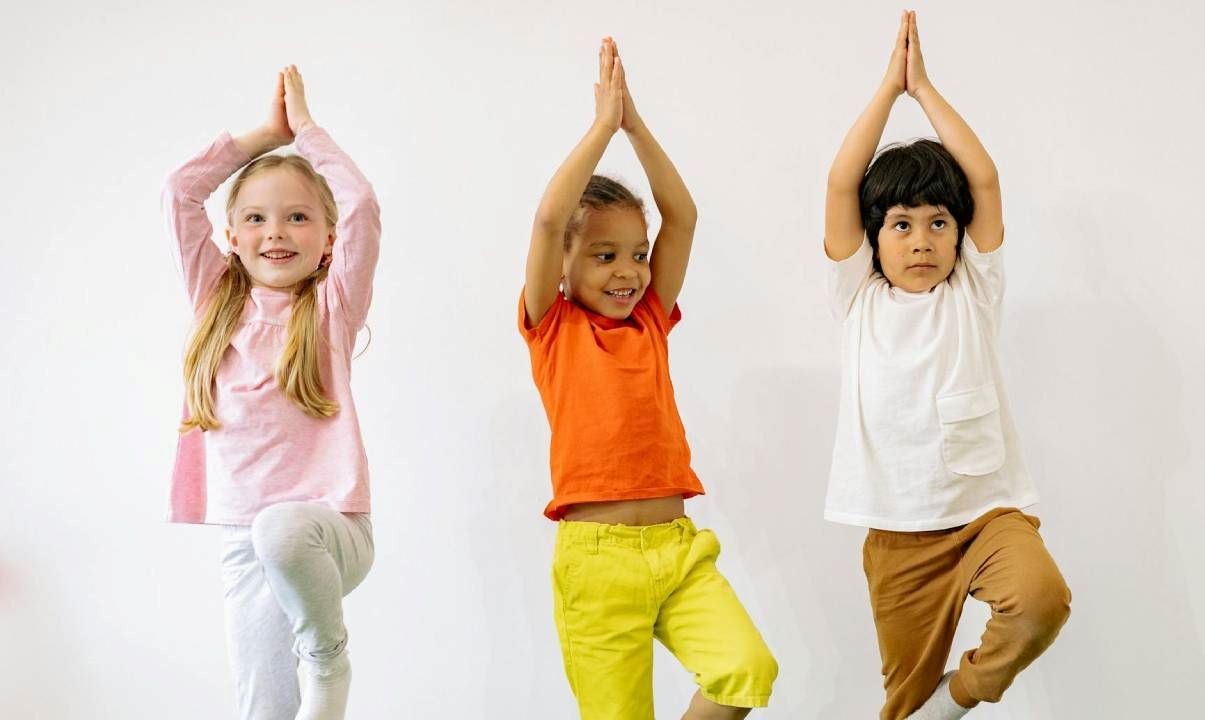 Three children doing the tree yoga pose against a white background