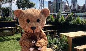 A person in a teddy bear costume standing next to a picnic blanket with Newcastle’s Millennium Bridge in the background