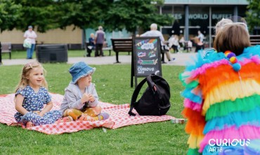 A person in a brightly coloured outfit entertaining two toddlers