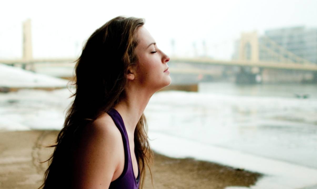 A woman doing Pilates on an exercise mat against a riverscape backdrop