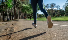 A woman running along a road in a grassy park with trees